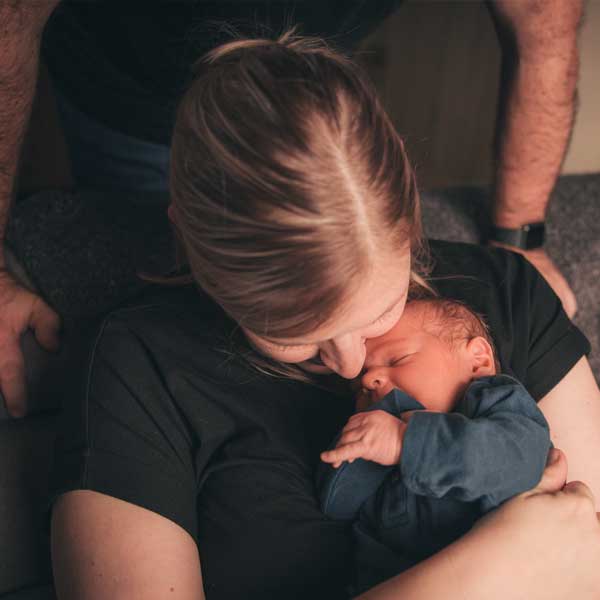 Mutter hält ihr schlafendes Neugeborenes liebevoll im Arm, Vater legt schützend die Hand auf ihre Schulter – inniger Familienmoment