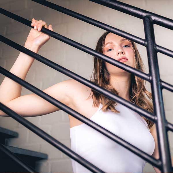 Junge Frau in weißem Top posiert hinter einem schwarzen Treppengeländer in modernem, urbanem Stil