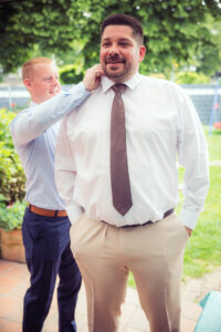 Der Bräutigam wird draußen beim Anziehen seiner Krawatte von einem Freund unterstützt