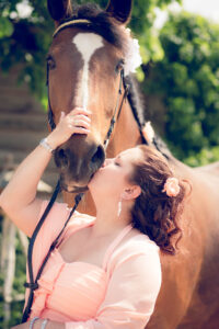 Die Braut in einem lachsfarbenen Kleid küsst liebevoll ihr Pferd an der Schnauze