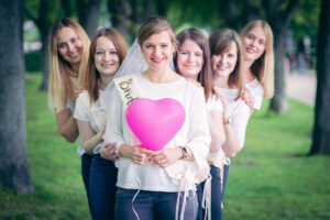 Die Braut hält einen pinken Herzluftballon, umgeben von ihren Freundinnen bei einem Junggesellinnenabschied im Park