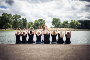 Gruppe von Frauen mit schwarzen Shirts formt Herzen mit den Händen am Seeufer beim Junggesellinnenabschied