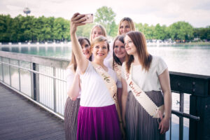 Eine Braut macht mit ihren Freundinnen ein Selfie beim Junggesellinnenabschied auf einer Holzbrücke am See