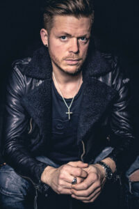 Mann mit Lederjacke und Kreuzkette in dramatischer Lichtstimmung – intensives Portraitshooting